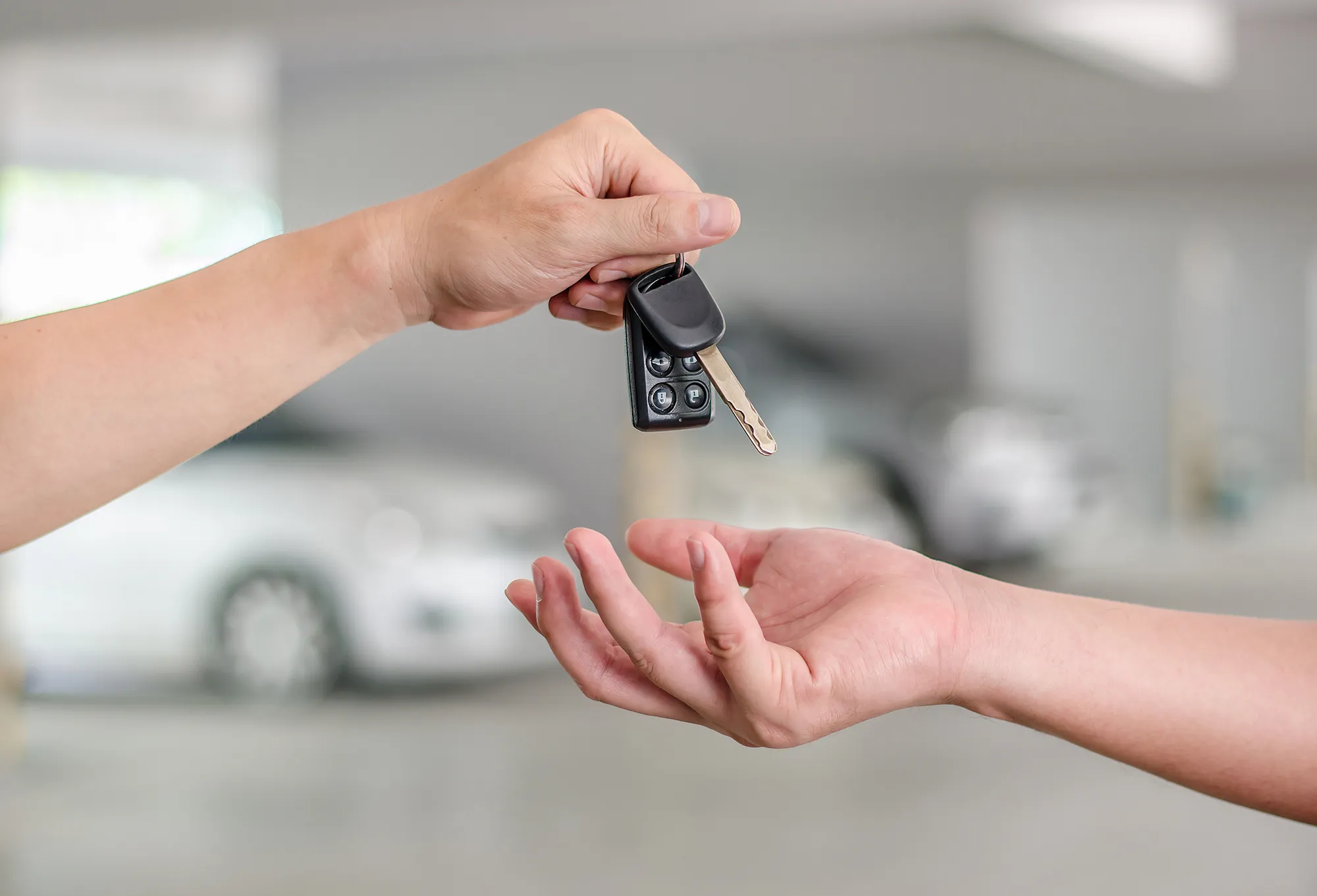Male hand holding a car key and handing it over to another perso Person receiving new car keys